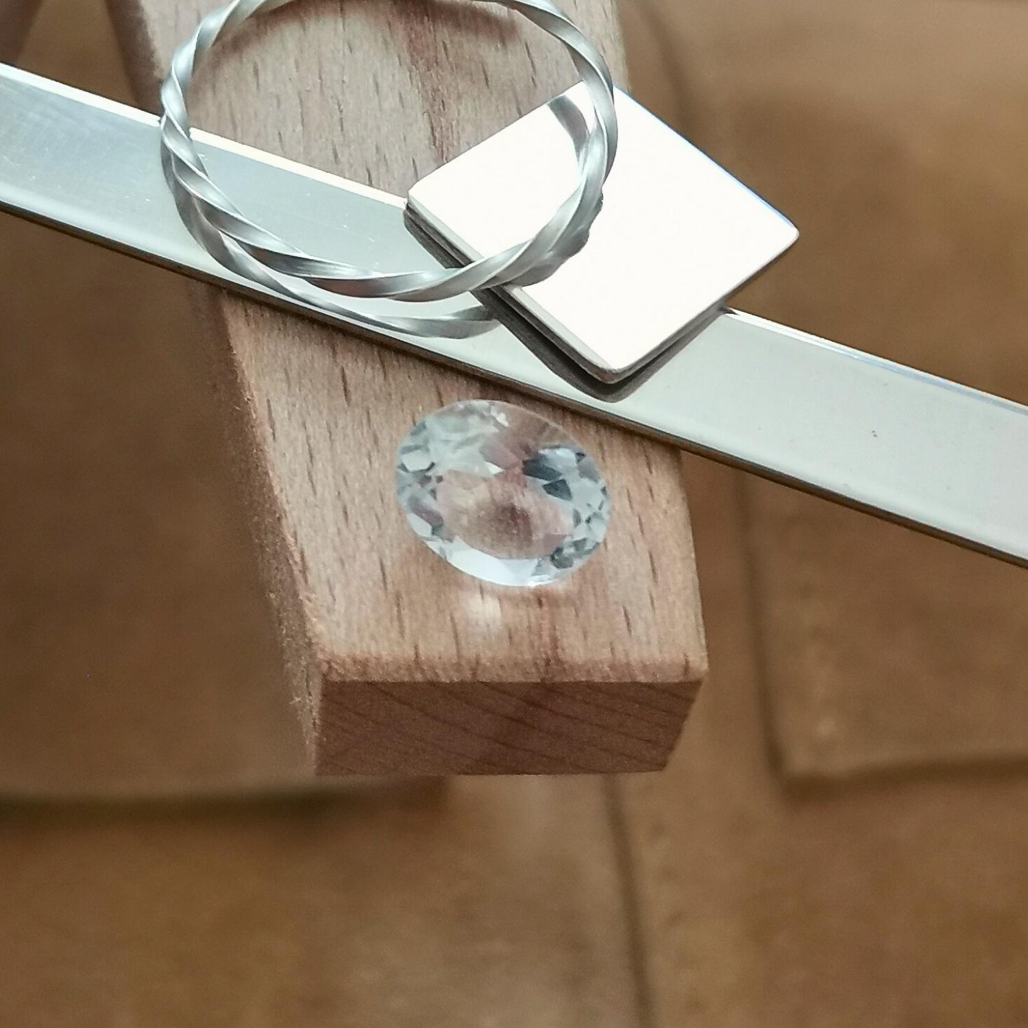 The clear quartz oval displayed on a jewellers bench peg with some sterling silver sheet and wire.