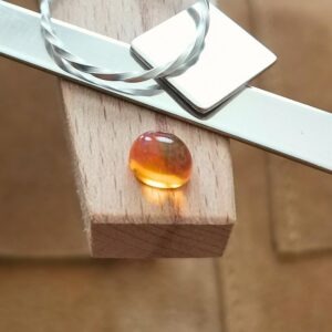 The fire opal oval cabochon displayed on a jewellers bench peg with some sterling silver sheet and wire.