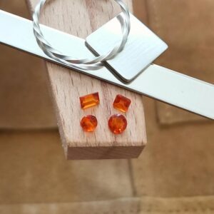 The four small orange tourmaline gemstones displayed on a jewellers bench peg with some sterling silver sheet and wire.