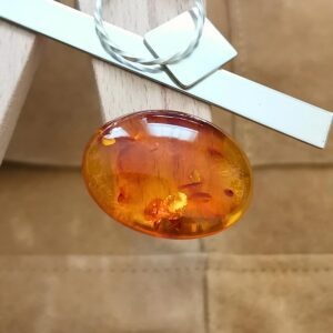 The rich orange amber cabochon oval displayed on a jewellers bench peg with some sterling silver sheet and wire.