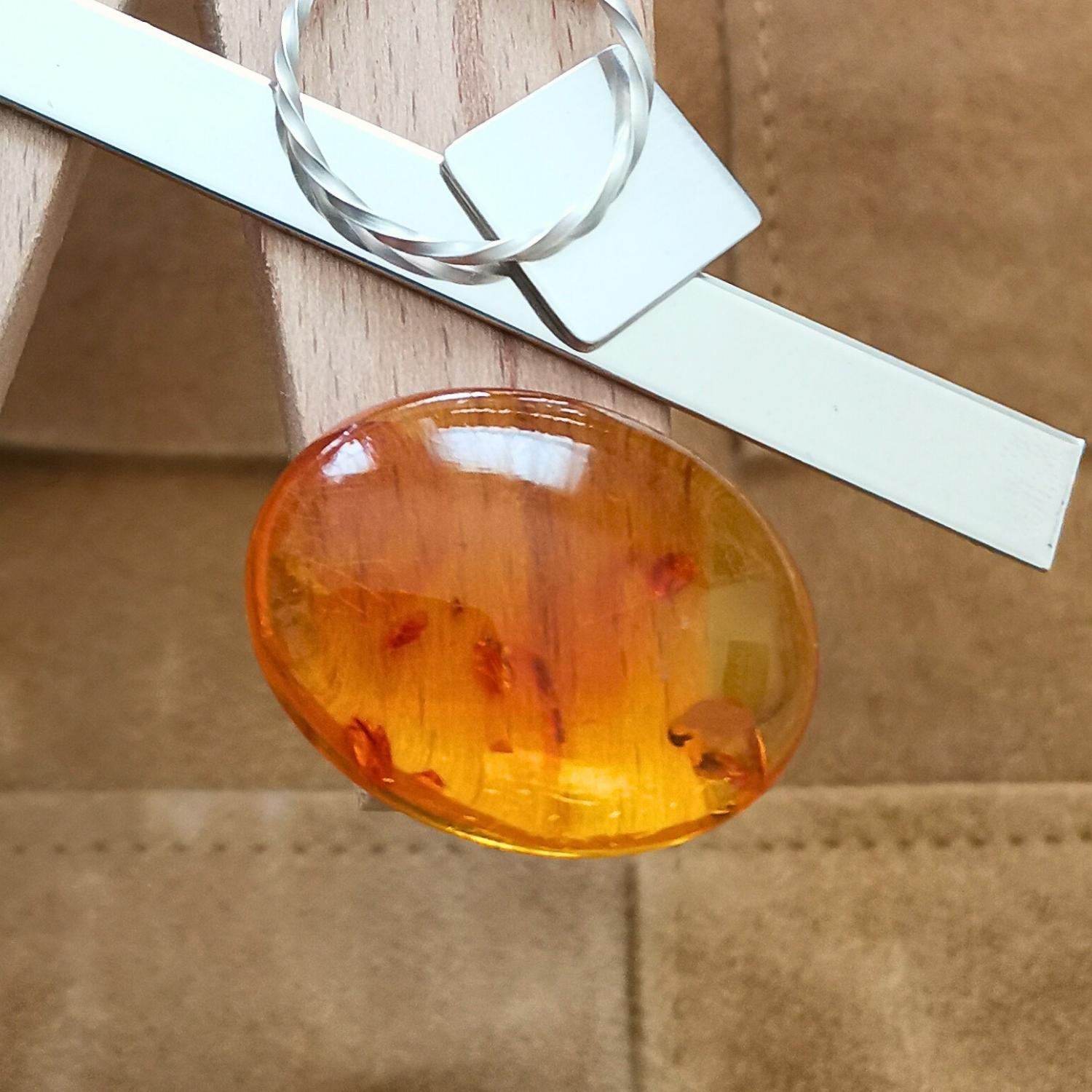 The golden amber cabochon oval displayed on a jewellers bench peg with some sterling silver sheet and wire.