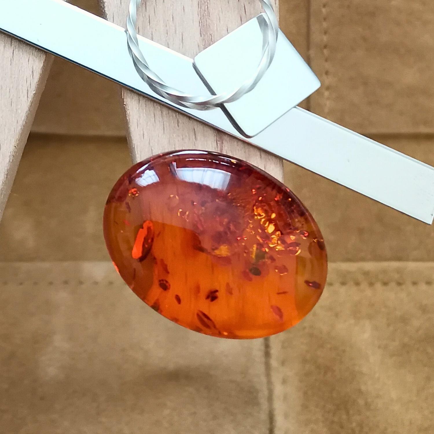 The large included oval amber cabochon displayed on a jewellers bench peg with some sterling silver sheet and wire.