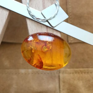 The larhe orange amber cabochon oval displayed on a jewellers bench peg with some sterling silver sheet and wire.