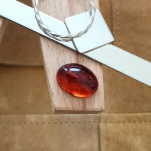 The dark orange oval amber cabochon displayed on a jewellers bench peg with some sterling silver sheet and wire.
