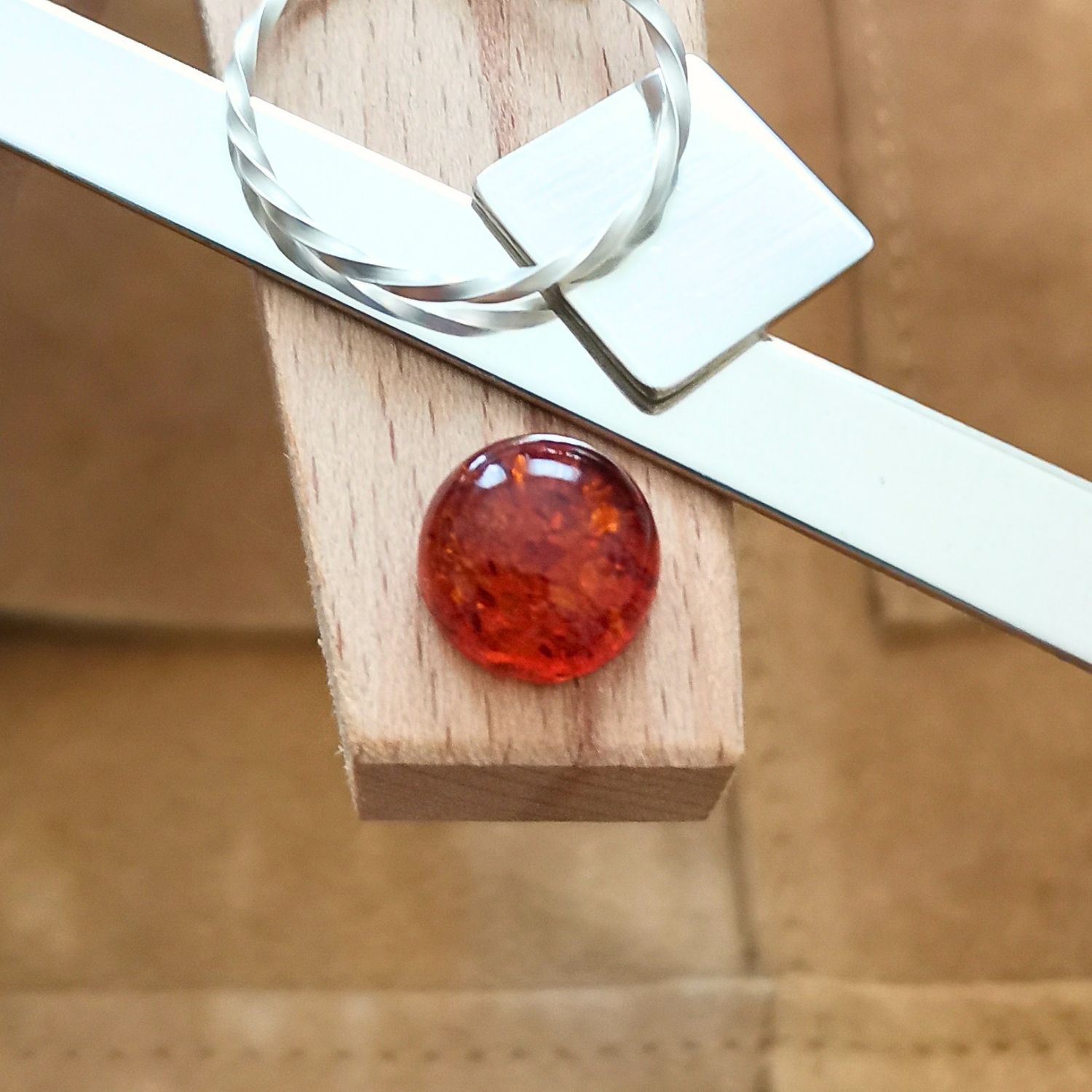 The round orange amber cabochon displayed on a jewellers bench peg with some sterling silver sheet and wire.