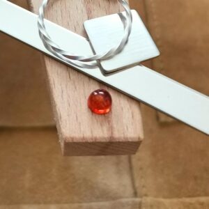The the small round amber cabochon displayed on a jewellers bench peg with some sterling silver sheet and wire.