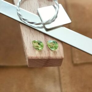 The pair of small peridot teardrops displayed on a jewellers bench peg with some sterling silver sheet and wire.