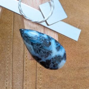 The loose teardrop dendritic agate cabochon is being displayed on a wooden jewellers bench peg with some sterling silver sheet and wire.