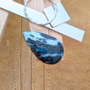 The loose teardrop dendritic agate cabochon is being displayed on a wooden jewellers bench peg with some sterling silver sheet and wire.