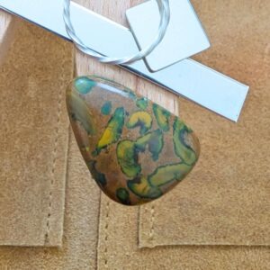 The loose freeform fruit jasper cabochon is being displayed on a wooden jewellers bench peg with some sterling silver sheet and wire.