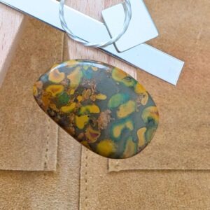 The loose freeform fruit jasper cabochon is being displayed on a wooden jewellers bench peg with some sterling silver sheet and wire.