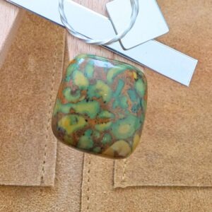 The loose square fruit jasper cabochon is being displayed on a wooden jewellers bench peg with some sterling silver sheet and wire.