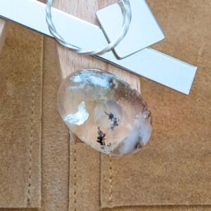 The loose oval dendritic opal cabochon is being displayed on a wooden jewellers bench peg with some sterling silver sheet and wire.