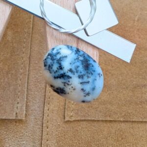 The loose dendritic opal cabochon is being displayed on a wooden jewellers bench peg with some sterling silver sheet and wire.