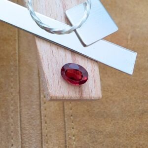 The loose faceted red garnet oval is being displayed on a wooden jewellers bench peg with some sterling silver sheet and wire.