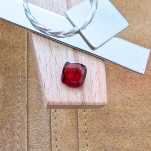 The loose faceted red garnet square is being displayed on a wooden jewellers bench peg with some sterling silver sheet and wire.